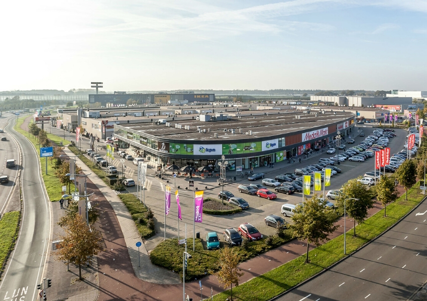 Groot winkelcomplex met verschillende retailers aan periferie en geparkeerde auto's